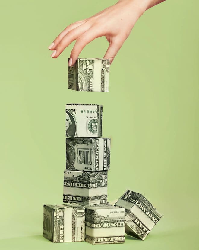 A hand carefully placing a folded banknote cube on top of a stacked tower